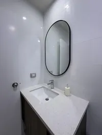 Lavatorio del baño propio con espejo ovalado y tablero de cuarzo